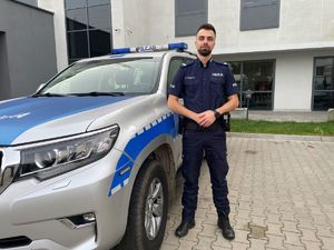 Policjant na tle radiowozu.