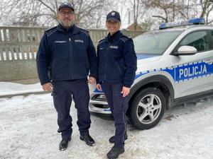 Umundurowani policjanci stoją przed radiowozem.