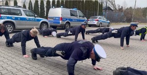 Policjanci wykonujący pompki, w tle radiowozy.
