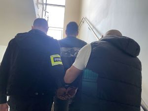 Zatrzymany mężczyzna trzymany przez dwóch funkcjonariuszy.