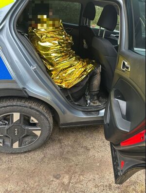 Kobieta w otwartym radiowozie okryta kocem termicznym.