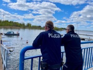Dwaj policjanci patrzący na wodę, w tle łódź policyjna.