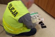 policjant w odblaskowej kamizelce z napisem policja  ogląda zabezpieczone narkotyki