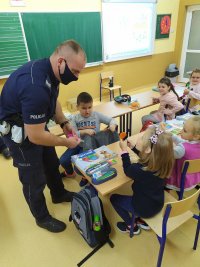 policjant rozdający odblaski dzieciom w szkolnych ławkach