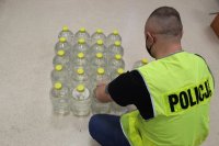 Policjant  kuca przy butelkach i spisuje nielegalny alkohol, który leży na ziemi.