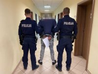 Dwaj policjanci ubrani w granatowy mundur prowadzą jedną z trzech zatrzymanych osób