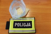 Plastikowy woreczek, w którym znajduje się 40 gramów amfetaminy, obok leży odblaskowa opaska z napisem policja.