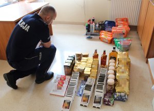 Policjant ubrany w granatowy mundur rozłożył na podłodze skradzione towary i będzie je spisywać.