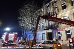 miejsce akcji gaśniczej, strażacy gaszą pożar kamienicy, na ulicy stoją wozy strażackie