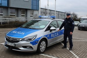 policjant, który uratował 13-letnią dziewczynkę, stoi przy radiowozie, w tle budynek komendy policji