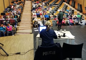 Sala kinowa w Ratuszu, na widowni seniorzy, na scenie policjantka podczas wykładu