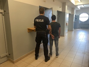 zatrzymany sprawca kradzieży wprowadzany przez policjanta do pomieszczenia dla osób zatrzymanych