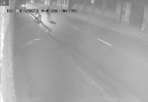 Zdjęcie jest zrzutem ekranu z monitoringu. Jest noc. W górnym lewym rogu widać datę 01.2023 godzina 20:36:35,  widać jedną osobę stojąca przy wózku inwalidzkim, a drugą siedząca na wózku.