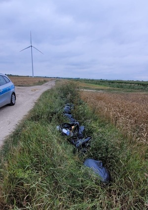 W rowie, miedzy drogą, a uprawnym polem, leżą w rzędzie czarne worki ze śmieciami. Po lewej stronie stoi radiowóz.