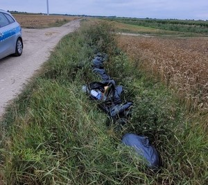 W rowie, między drogą, a polem uprawnym, leżą czarne worki ze śmieciami. Po lewo stoi radiowóz.