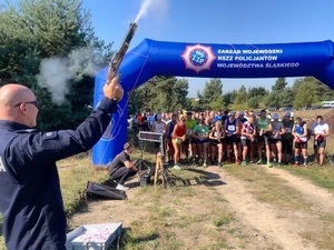 Linia startu, zawodnicy ustawieni przed linią, po lewej stronie stoi policjant w mundurze, daje sygnał do startu.