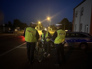 Policjanci podczas kontroli drogowej wręczają rowerzystce kamizelkę odblaskową.