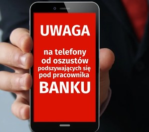 Osoba trzymająca telefon, pokazuje jego ekran. Na czerwonym tle, białymi literami jest napis: &quot;Uwaga na telefony od oszustów podszywających się pod pracownika banku&quot;.