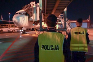 Dwaj policjanci w kamizelkach z napisem policja, stoją przed samolotem