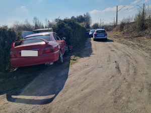 Po lewej stronie stoi tyłem do zdjęcia samochód, dalej po prawej stronie widać stojące wzdłuż drogi dwa radiowozy.