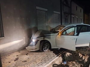Samochód wbił się w ścianę budynku, w środku są poduszki powietrzne, auto ma otwarte drzwi od strony kierującego.