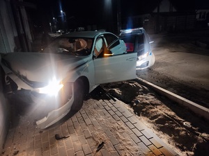 Samochód wbił się w ścianę budynku, w środku są poduszki powietrzne, auto ma otwarte drzwi od strony kierującego. Z tyłu za samochodem stoi radiowóz.