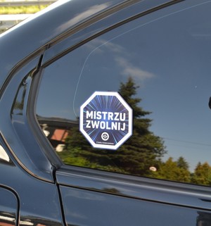 Na szybie samochodu przyklejona jest naklejka "Mistrzu zwolnij".