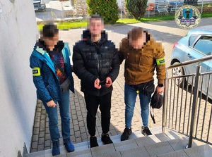 Dwoje policjantów prowadzi po schodach zatrzymanego na komendę. Wchodzą bo budynku od strony podwórka.