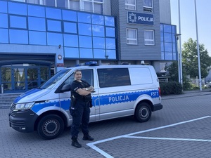 Umundurowana policjantka, stojąca przy oznakowanym radiozie na tle budynku komendy w Zduńskiej Woli.