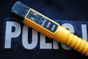 zdjęcie poglądowe. Na masce granatowym podłożu z napisem POLICJA leży urządzenie w kolorze żółtym do stwierdzenia obecności alkoholu w organizmie.