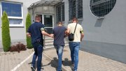 dwóch policjantów po cywilnemu prowadzi zatrzymanego na dziedzińcu komendy