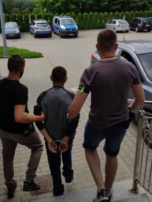 dwaj policjanci po cywilnemu prowadza po schodach dziedzińca komendy zatrzymanego meżczyznę