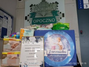 zdjecia paczki dla maluszka, w pudełku ułożone są artykuły higieniczne dla dzieci  zastępca komendanta odbiera podziekowanie z rąk koordynatorki projektu, pudełko z plakatem z napisem paczka dla maluszka  podziekowanie w ramce