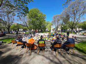 czytanie dzieciom na placu Kościuszki, dzieci siedzą koło fontanny, słuchają czytanych bajek. Policjant , strażak i mężczyzna siedzą na krzesłach