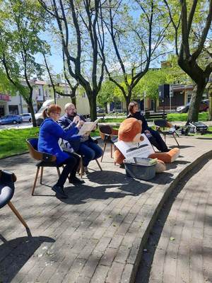 czytanie dzieciom na placu Kościuszki, dzieci siedzą koło fontanny, słuchają czytanych bajek. Policjant , strażak i mężczyzna siedzą na krzesłach