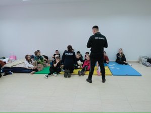 spotkanie z dziećmi w OSP w Kunicah, dzieci siedzą na materacach, policjant i strażak  rozmawiają z nimi