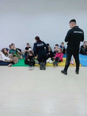 spotkanie z dziećmi w OSP w Kunicah, dzieci siedzą na materacach, policjant i strażak  rozmawiają z nimi