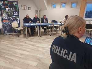 debata w Brudzewicach, Brąszewicach mieszkańcy siedzą przy stole , policjanci rozmawiają z mieszkańcami w tle baner policji z napisem Zostań Jednym z nas  i gminy Poświętne