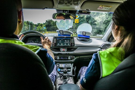 policjanci siedzą w radiowozie, na kokpicie leżą czapki policyjne.