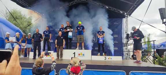trzech mężczyzn stoi na podium wokół nich stoi grupa ludzi, za nimi dym.