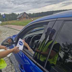 niebieski samochód, policjant wręcza ulotkę z napisem mistrzu zwolnij.