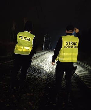 policjant i strażnik ochrony kolei stoją na torach.