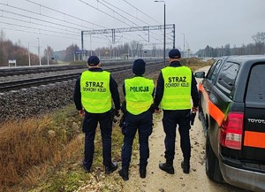 policjantka i dwóch strażników ochrony kolei stoją przy torach, obok samochód.