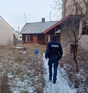 policjant w mundurze idzie w kierunku drewnianego domu.