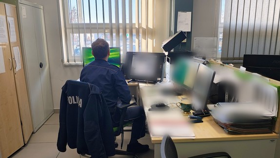 policjant siedzi tyłem, widoczne biurka i komputery.