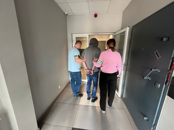 kobieta i mężczyzna z opaskami na rękach z napisem policja prowadzą męzczyznę.