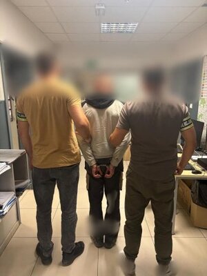 trzech mężczyzn, jeden ma założone kajdanki, dwóch innych ma na ręce napis policja.