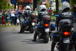 Funkcjonariusze z wydziału ruchu drogowego siedzą na motocyklach policyjnych, za nimi stoją ludzie robiący zdjęcia policjantom.