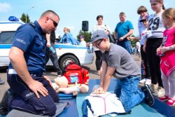 Policjant wydziału ruchu drogowego, podczas festynu uczy dzieci resuscytacji krążeniowo - oddechowej.